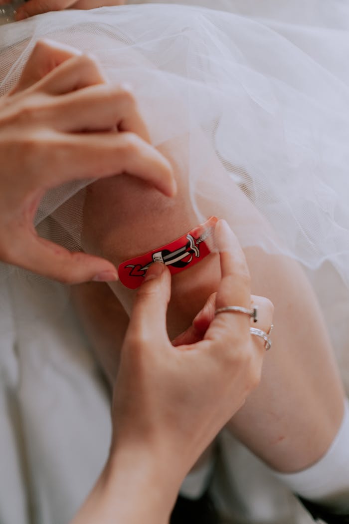Detailed shot of hands applying a red adhesive bandage to a knee, emphasizing care and healing.