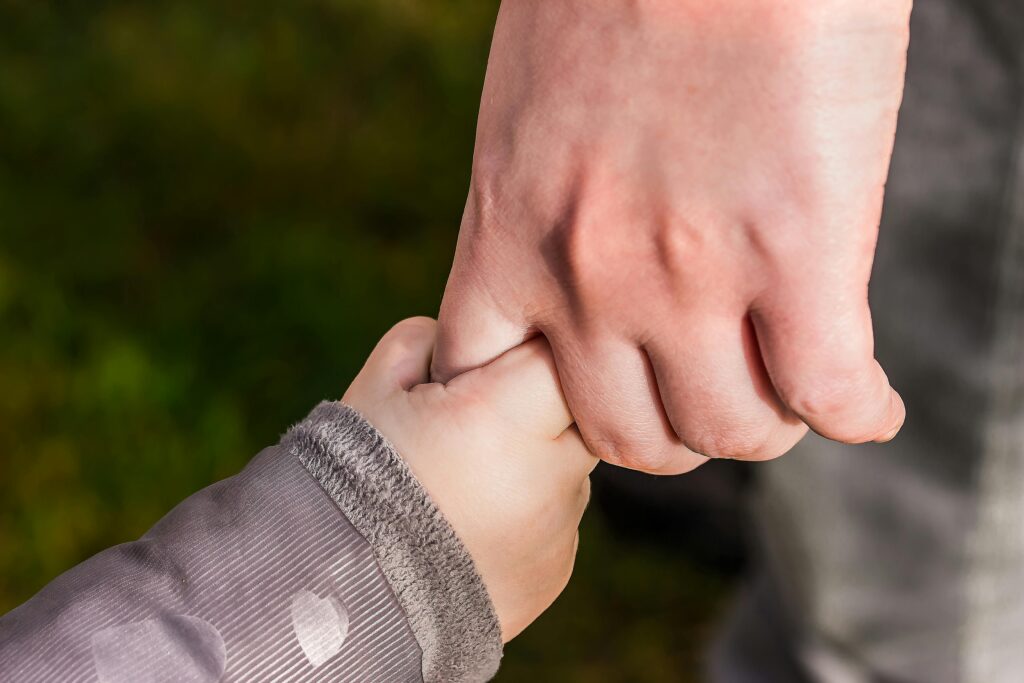 Das erwartet euch bei ResQKids A close-up of a child and parent holding hands in a park, symbolizing love and trust.