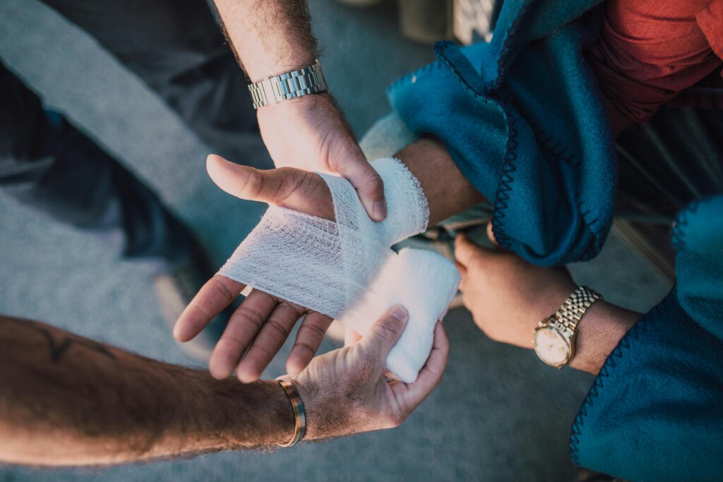 pexels photo 6519905 6519905 Close-up of two people bandaging an injured hand outdoors, focusing on first aid care.